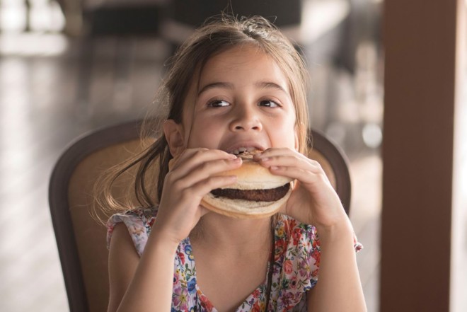 Child biting into a burger and holding with both hands